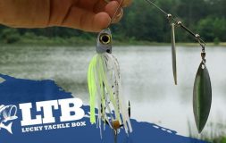 Hand holding a bait with yellow and white strips in front of a lake