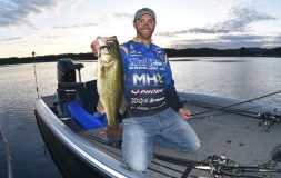 Man in the blue shirt holding big bass by the mouth on a boat