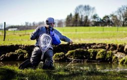 Man kneeling catching fish with a net on his back